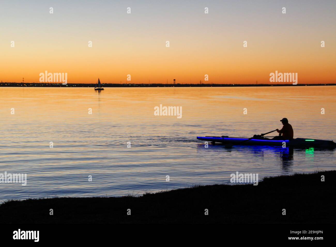 Un uomo solista pagaia un kayak vicino alla riva del lago Hefner al tramonto in una serata invernale. Foto Stock