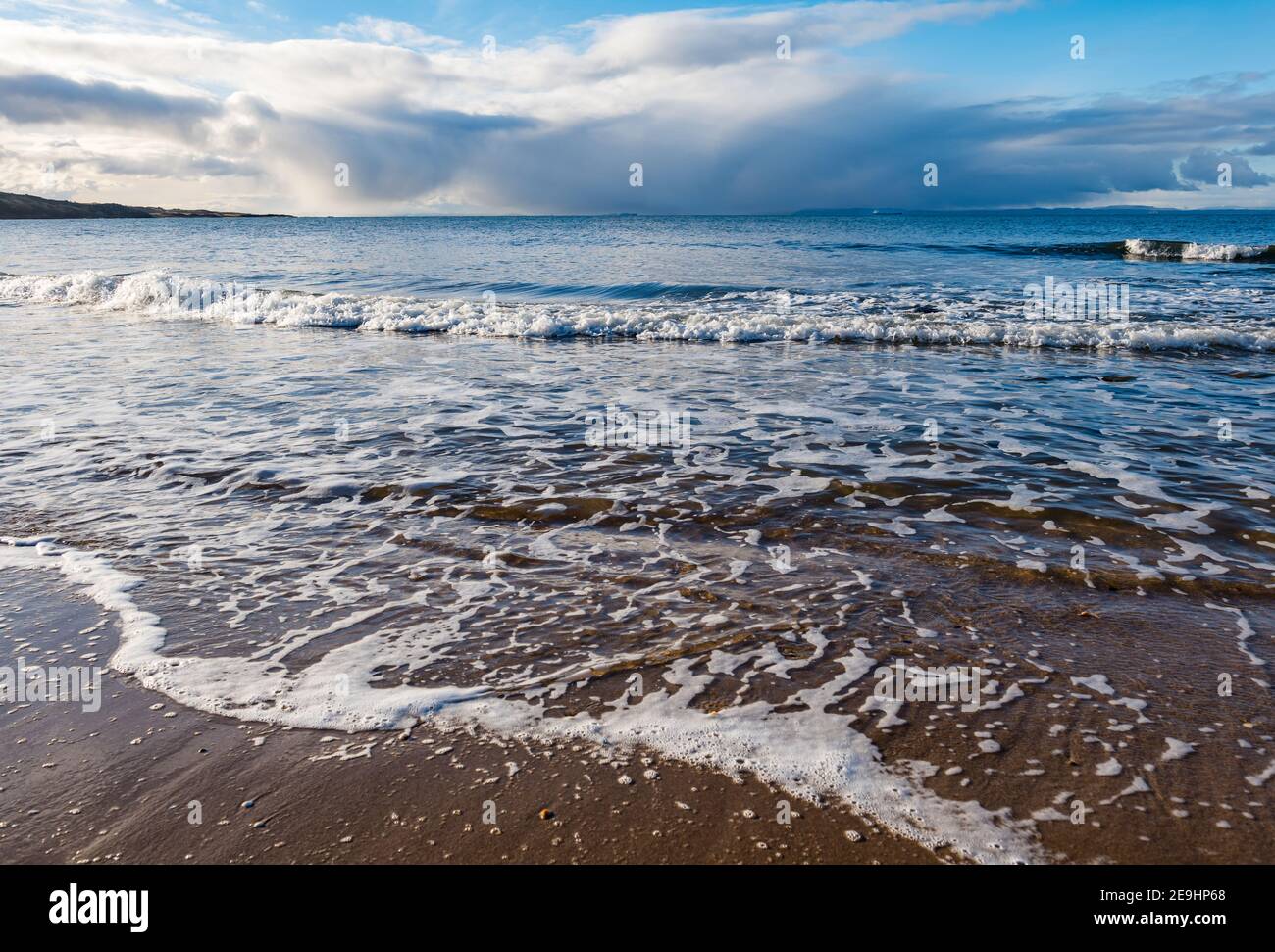 Onde sulla spiaggia di sabbia nella giornata di sole con il cielo tempestoso sul Firth of Forth Horizon, Gullane Beach, East Lothian, Scozia, Regno Unito Foto Stock