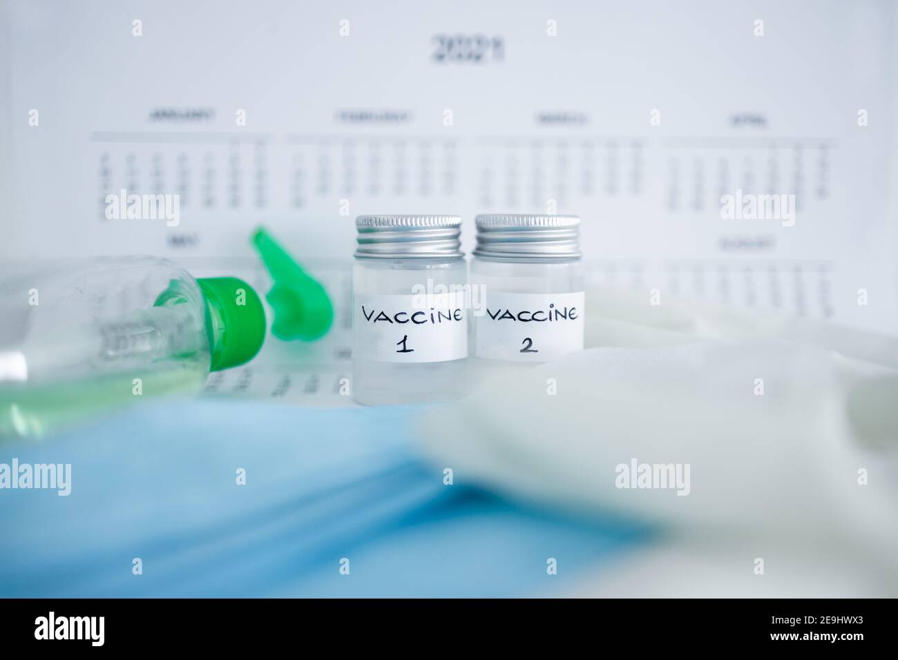 Vaccino covid-19 e immunizzazione contro la pandemia, ampolle con le etichette vaccino 1 e vaccino 2 affiancate accanto al calendario annuale 2021 e mas Foto Stock