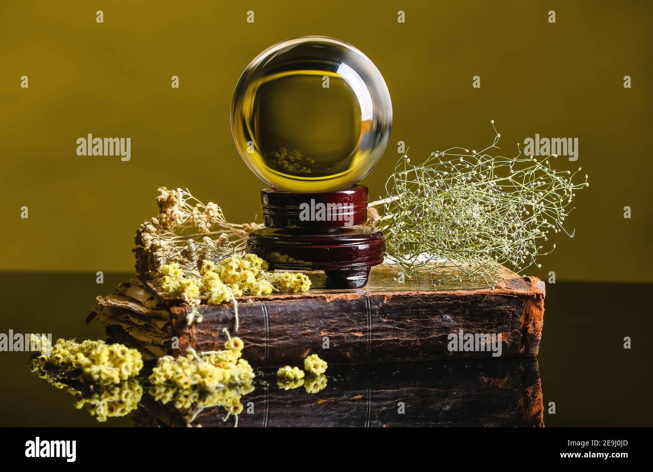 Palla di cristallo di cassiere di fortuna, libro ed erbe secche sul tavolo Foto Stock