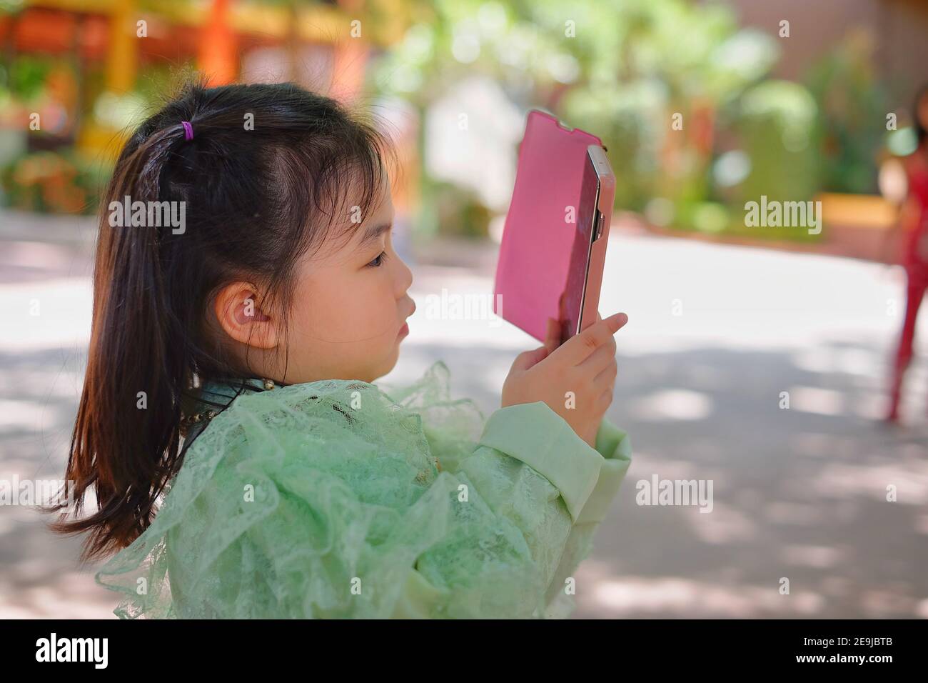 Una ragazza asiatica carina sta tenendo uno smartphone rosa, cercando di scattare una foto in vacanza. Foto Stock