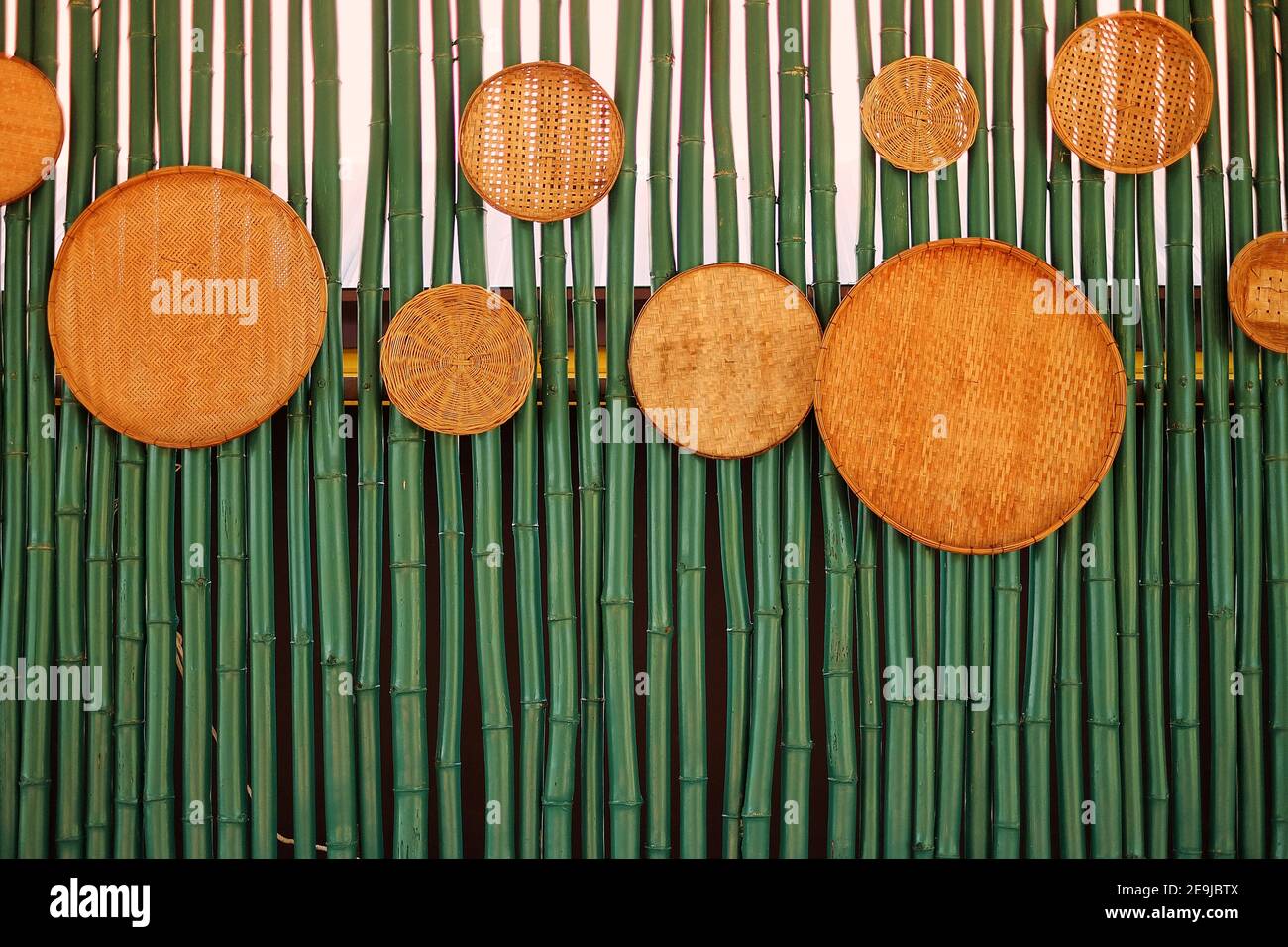 Una parete fatta di bambù verdi, decorata con tavole rotonde di bambù tessuta. Foto Stock