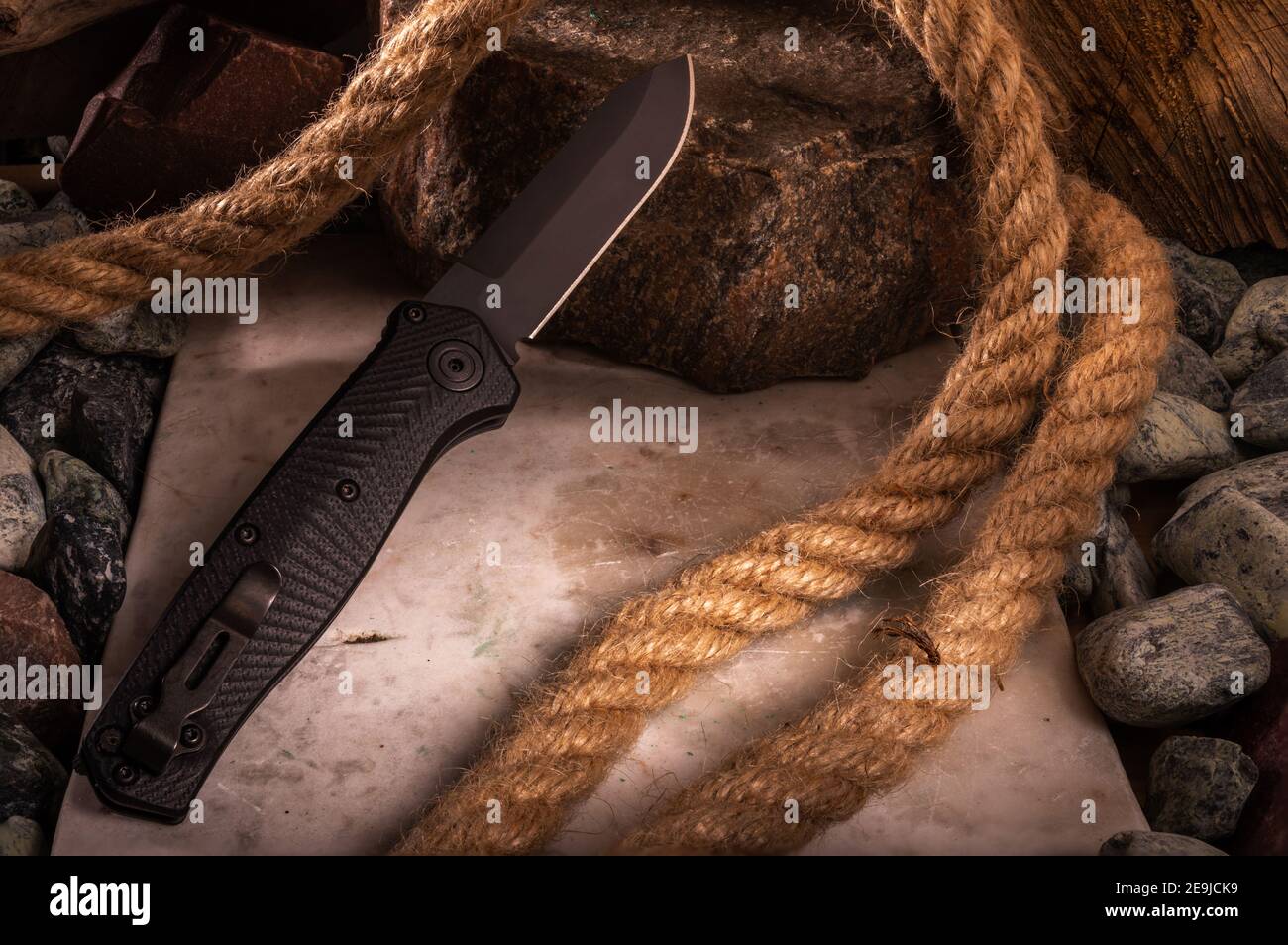 Il lato opposto del coltello con una clip sullo sfondo di pietre e corda. Foto di un coltello con una grande profondità di campo. Clip per il trasporto di una maglia Foto Stock
