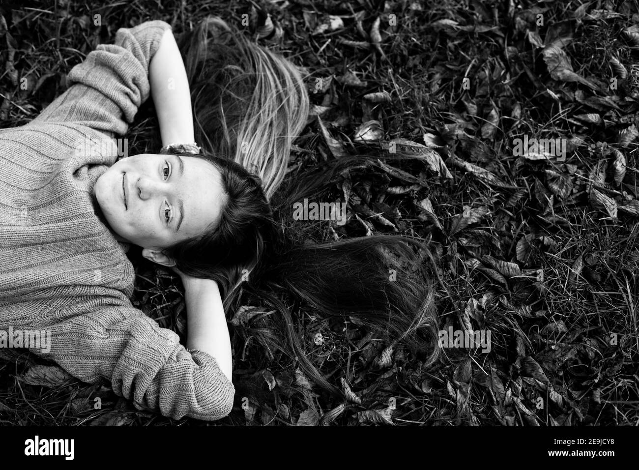 Ragazza teen che posa su terra autunnale con i capelli lunghi sparsi sull'erba. Foto in bianco e nero. Foto Stock