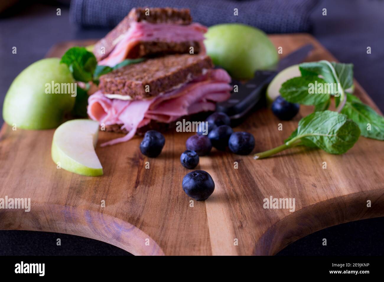 Panino integrale con prosciutto servito con fette di mele fresche e. mirtilli su una tavola di legno Foto Stock