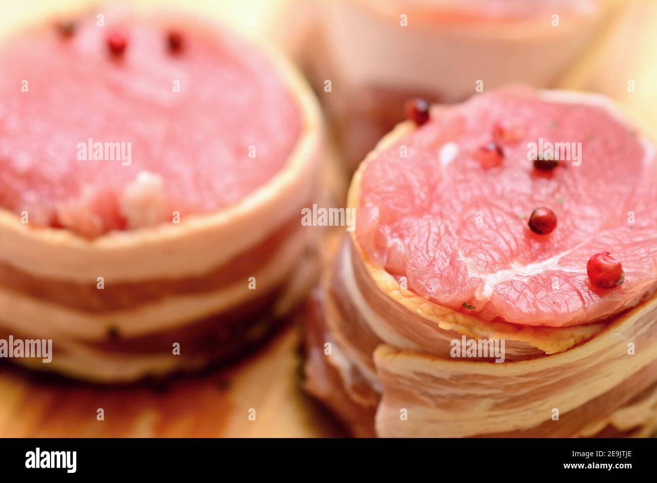 Closeup di medaglioni di filetto di maiale freschi e crudi con pancetta cosparsi di pepe rosso intero. Foto Stock