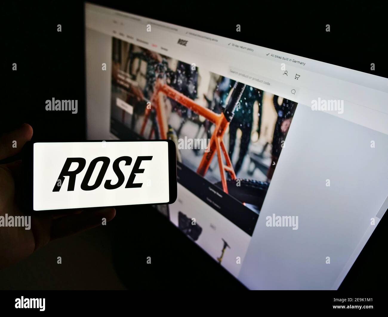 Persona che tiene il telefono cellulare con il logo del produttore tedesco di biciclette Rose Bikes GmbH in esposizione davanti alla pagina web. Mettere a fuoco sullo schermo del cellulare. Foto Stock