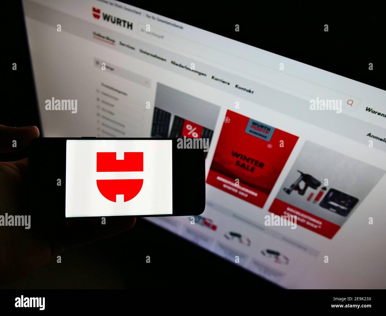 Vista ad alto angolo della persona che tiene il cellulare con il logo del conglomerato tedesco Würth Group in esposizione davanti al sito web. Mettere a fuoco lo schermo dello smartphone. Foto Stock
