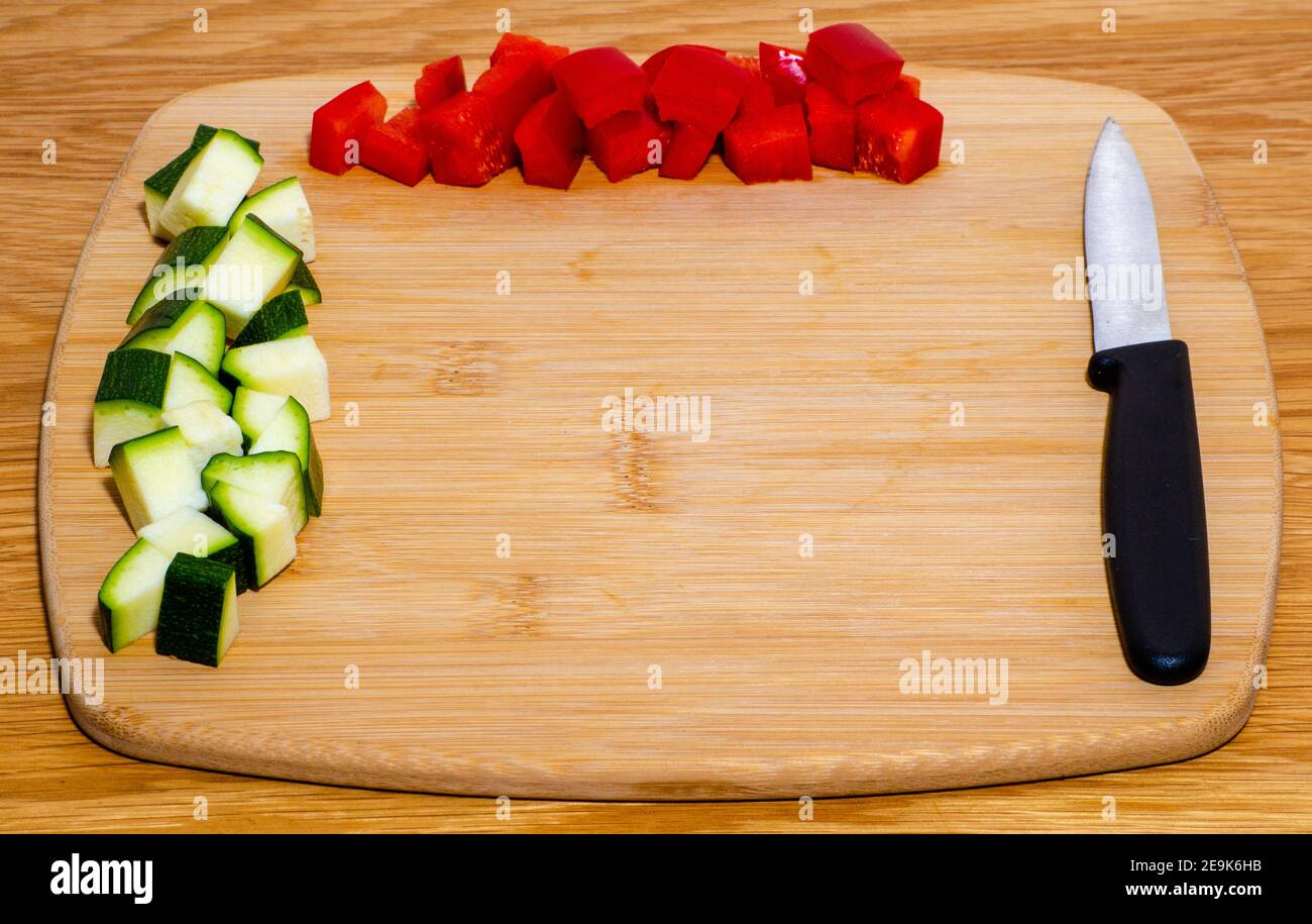Pepe a dadini e zucchine arrangiate su tagliere di legno con coltello e sfondo in legno con messa a fuoco selettiva e spazio di copia Foto Stock