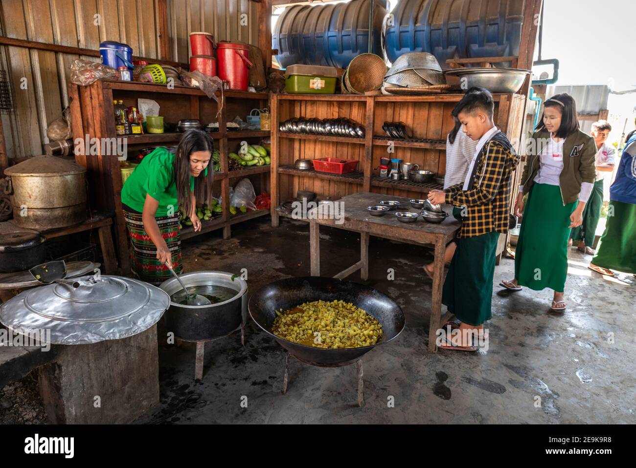 Gli studenti, la maggior parte dei quali sono orfani che sono fuggiti dalla guerra civile, vengono alla loro scuola di istruzione Chinpwi a Myikyina, Myanmar, durante la loro pausa pranzo. La direttrice, mai WGI lathe, distribuisce il cibo dai grandi pentole da cucina. Foto Stock