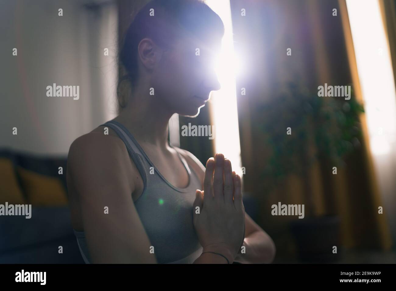 Colpo vicino di donna concentrata meditando al mattino con sole che splende attraverso la finestra Foto Stock