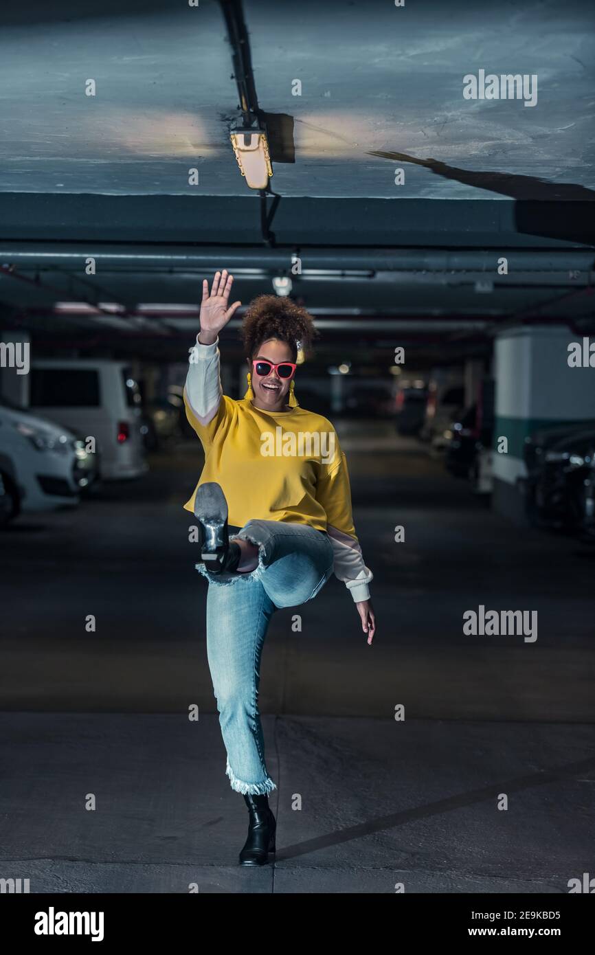 Corpo pieno di giovane donna afroamericana in trendy abbigliamento casual e  occhiali da sole che ondolano mano e saltano mentre hanno divertimento  sotterraneo Foto stock - Alamy