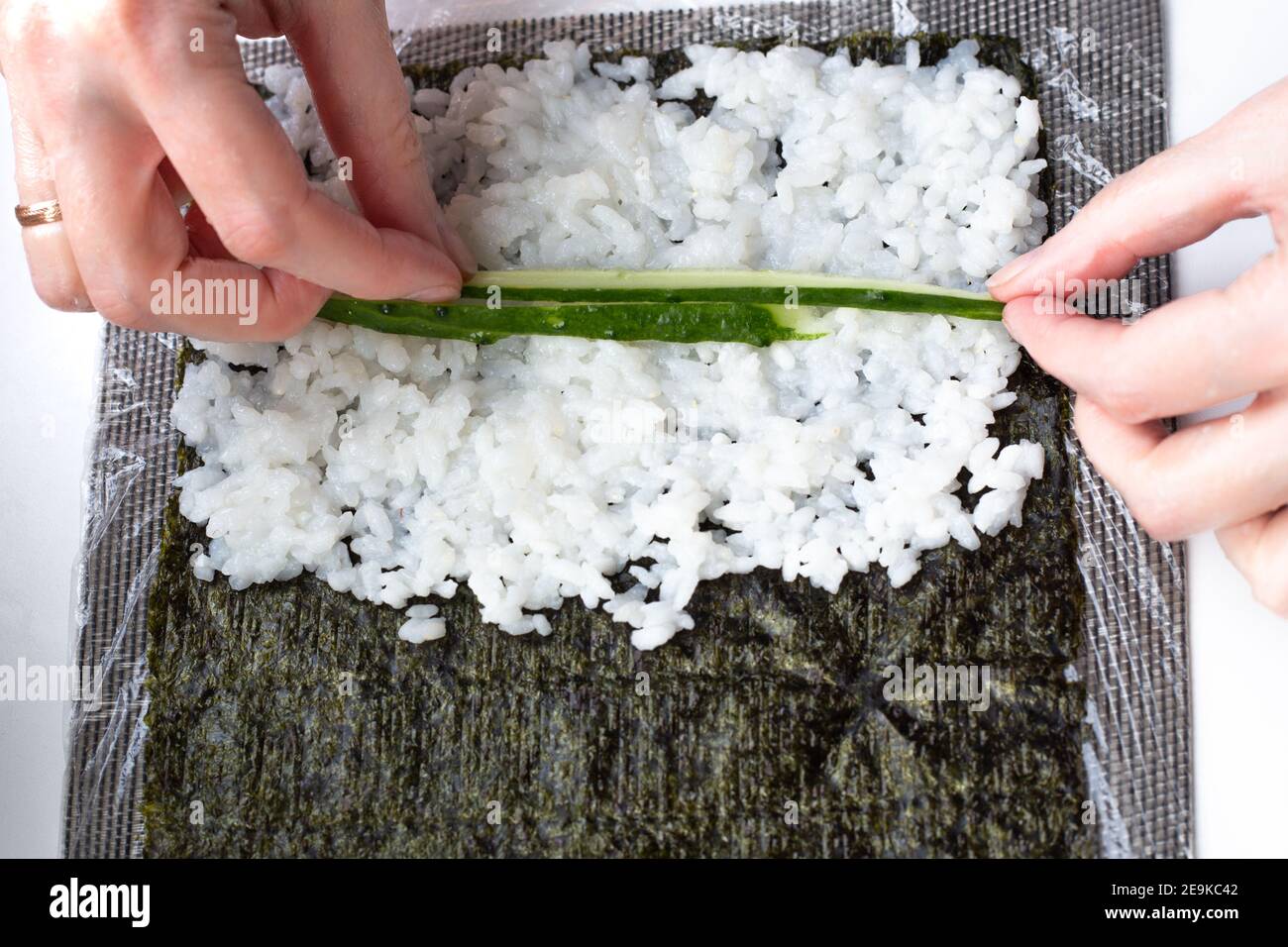 donna su una foglia di nori con riso stende strisce di cetriolo fresco verde. Cucina sushi, step3 Foto Stock