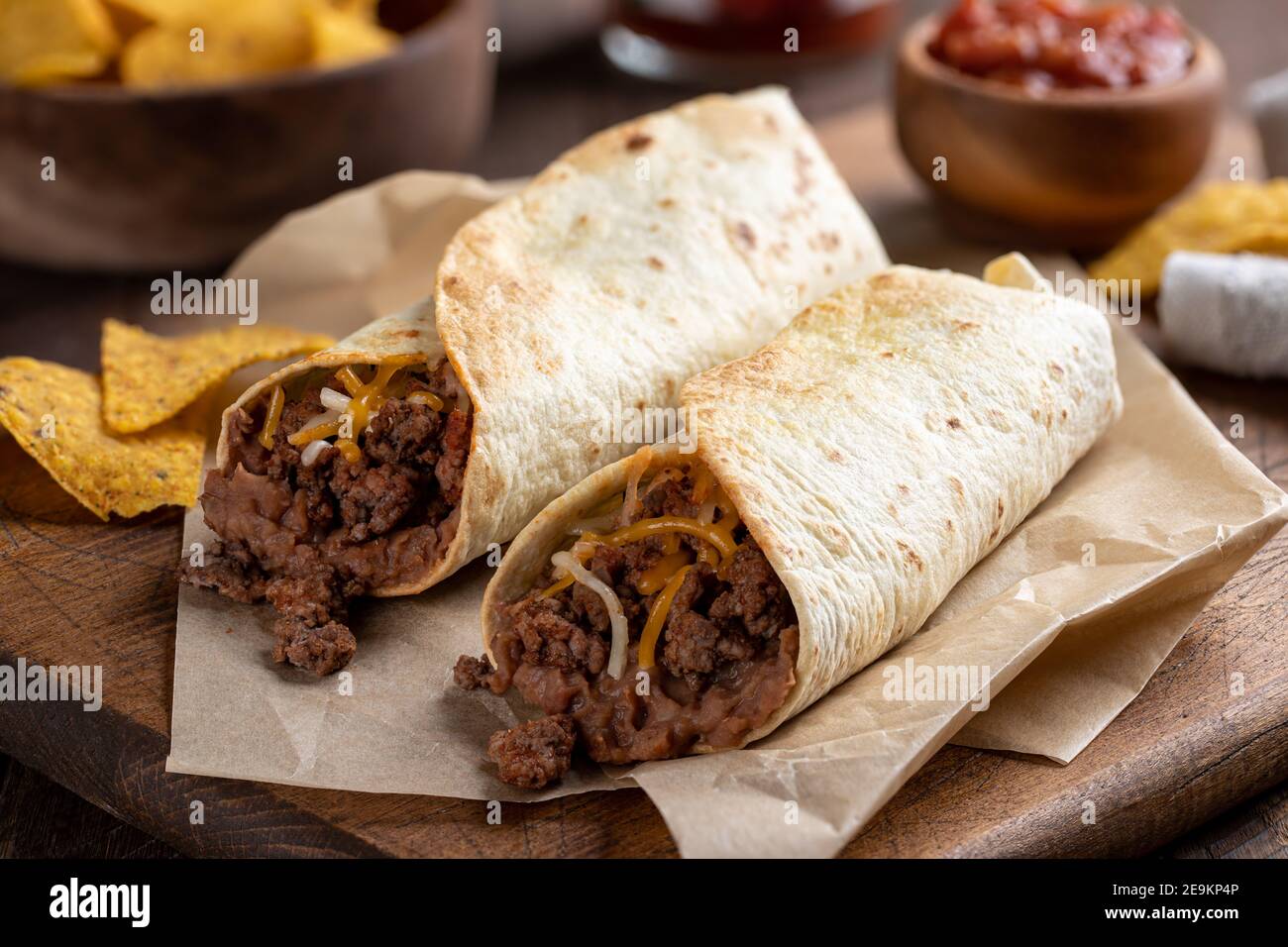 Burritos con manzo macinato, fagioli fritti e formaggio su un tagliere di legno Foto Stock