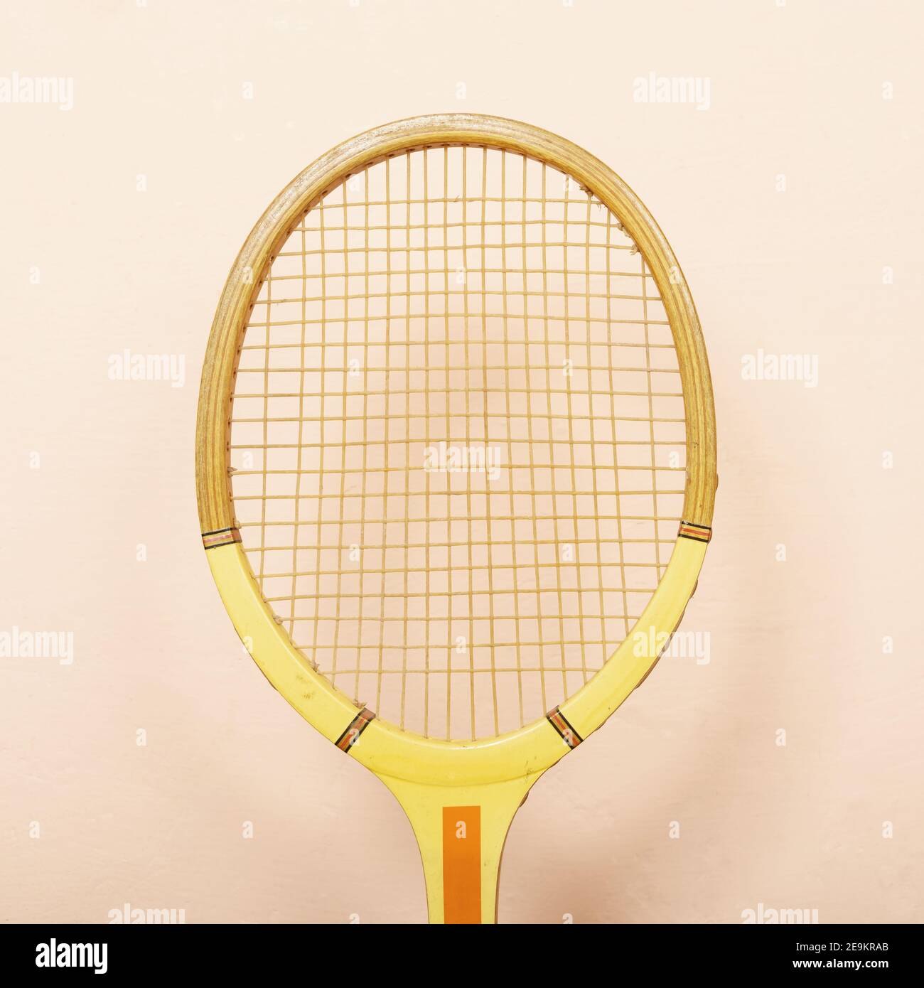 Racchetta da tennis in legno d'epoca contro le pareti rosa, tonalità pastello di giallo, arancione e rosa, concetto sportivo retrò Foto Stock