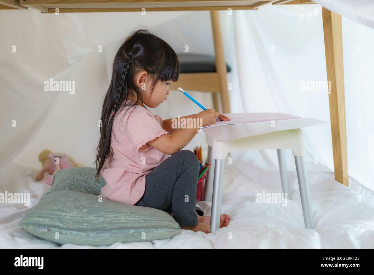 Asian cute bambina disegno in carta mentre si sdraiava in una coperta forte in soggiorno a casa per perfetto nascondersi dagli altri membri della famiglia Foto Stock