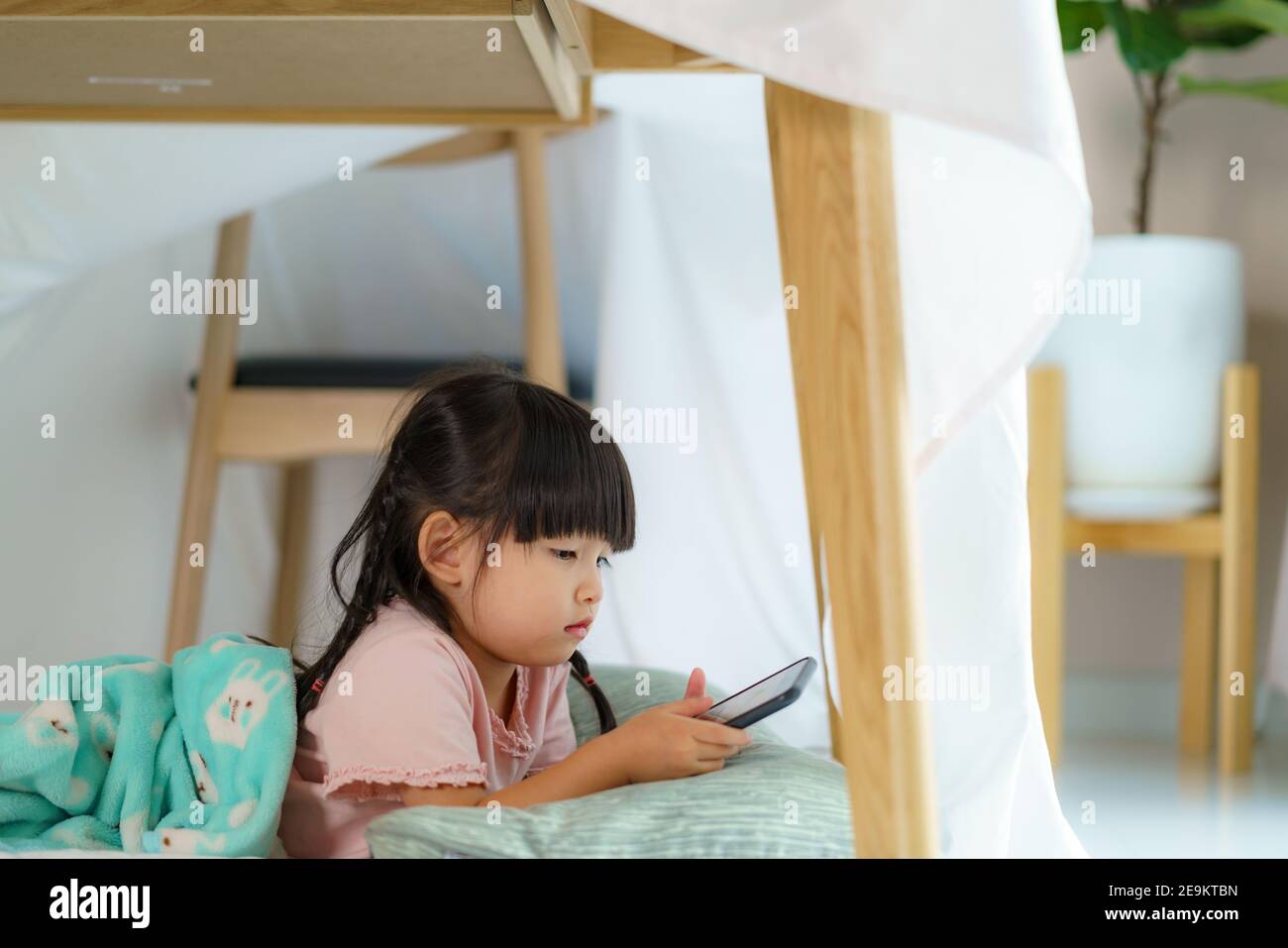 Asian cute bambina guardare cartone animato in smartphone mentre mentendo in un forte coperta in soggiorno a casa per perfetto nascondiglio lontano dal loro altro f Foto Stock