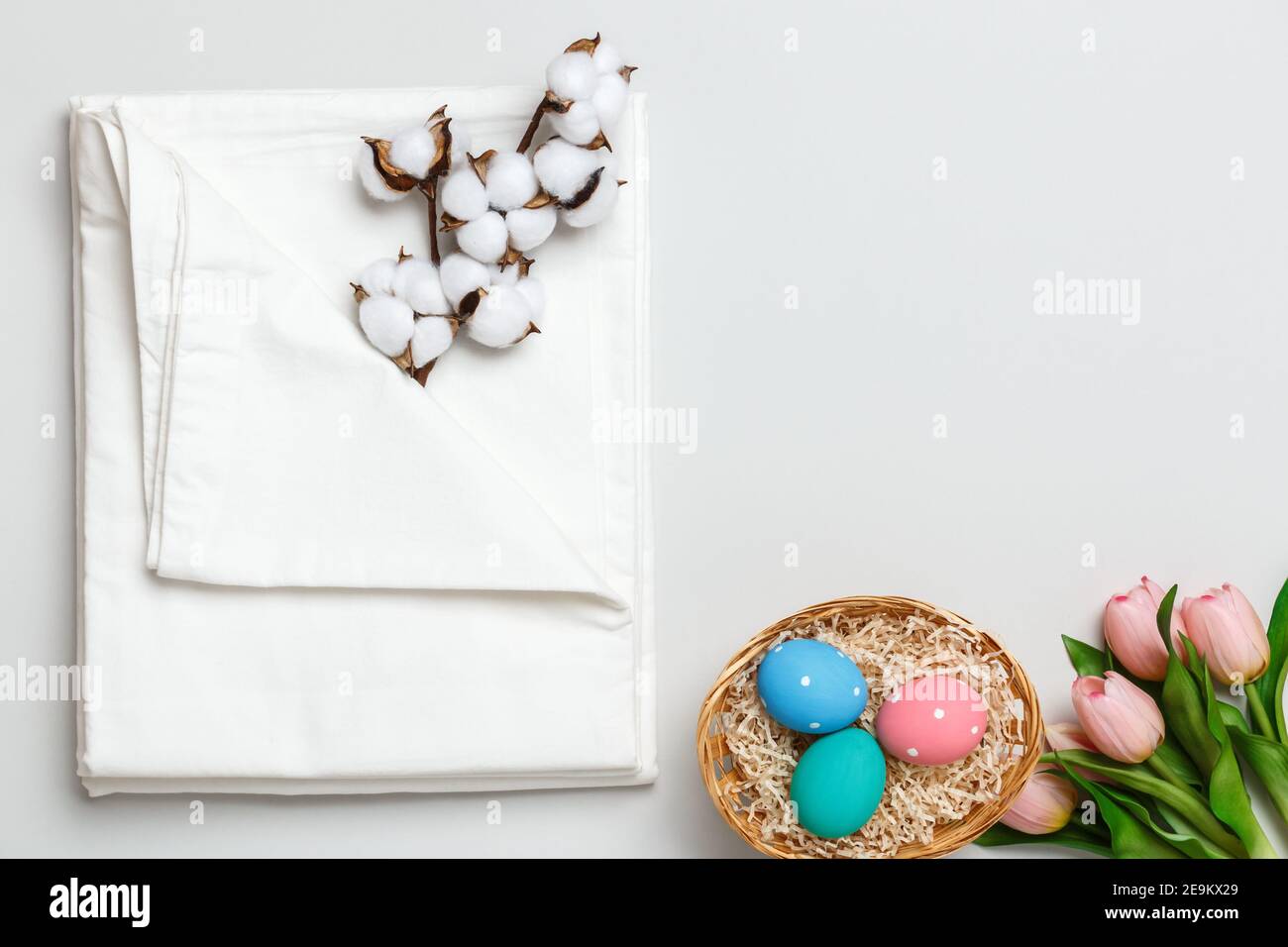 Vista dall'alto di una pila di lenzuola bianche, ramificazione di cotone e un cestino con uova di Pasqua. Spazio di copia. Foto Stock