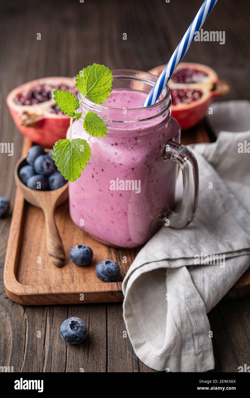 Frullato di melograno e mirtillo mescolato con yogurt e latte di mandorle, servito in un vaso di vetro su rustico sfondo di legno Foto Stock