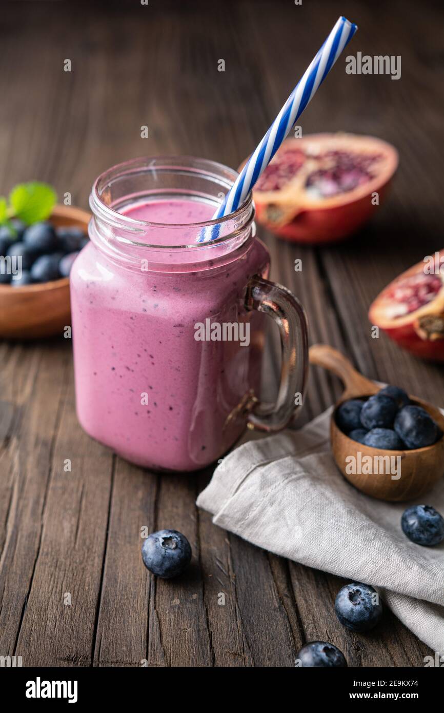 Frullato di melograno e mirtillo mescolato con yogurt e latte di mandorle, servito in un vaso di vetro su rustico sfondo di legno Foto Stock