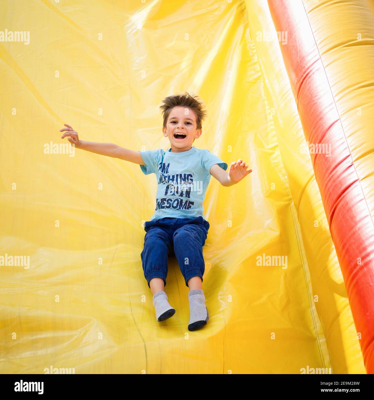 Ragazzo sorridente che gioca su uno scivolo gonfiabile Foto Stock