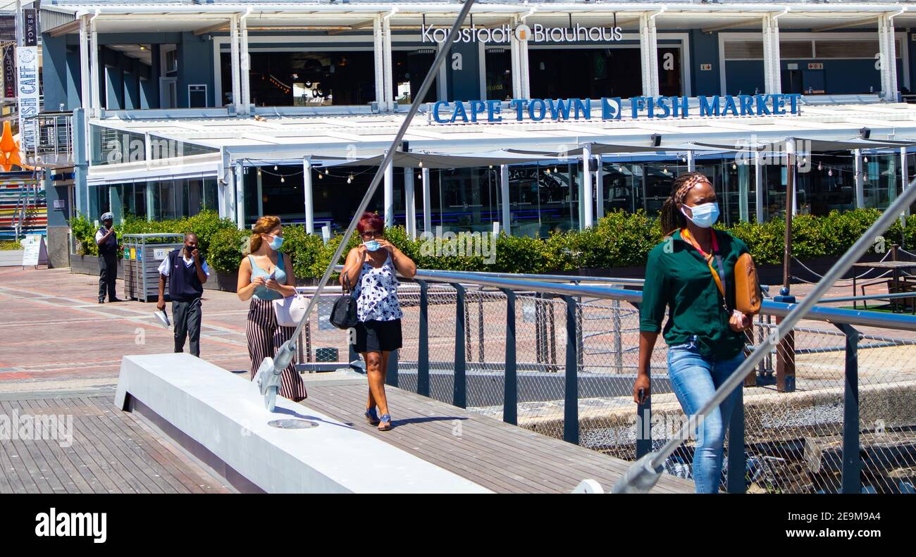 Waterfront - Città del Capo, Sud Africa - 03-02-2021 eleganti donne, coppie e guardia di sicurezza in maschere di faccia che camminano sopra l'attraversamento del ponte. Foto Stock