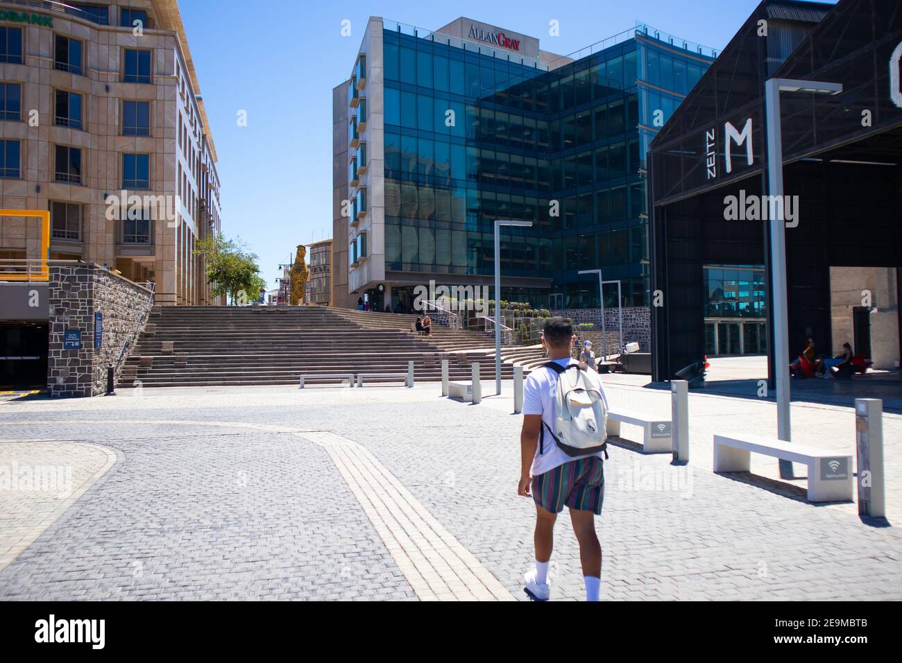 Waterfront - Città del Capo, Sud Africa - 03-02-2021 uomo che indossa la maschera a piedi verso il quartiere di Silo a Città del Capo. Panchine in primo piano. Foto Stock