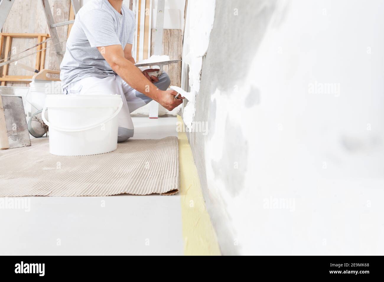 Mani uomo gesso di lavoro di costruzione lavoratore al lavoro closeup, prende gesso da secchio e lo mette su cazzuola per intonacare il muro, all'interno del cantiere Foto Stock