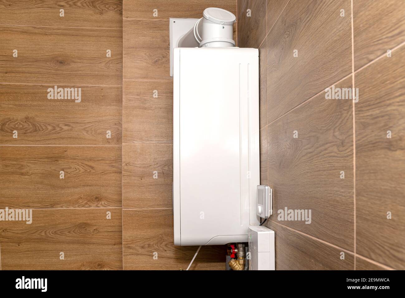 Una moderna caldaia a gas per gas naturale, installata in un locale caldaia rivestito di piastrelle in ceramica, tubo visibile che conduce il gas di scarico al camino. Foto Stock