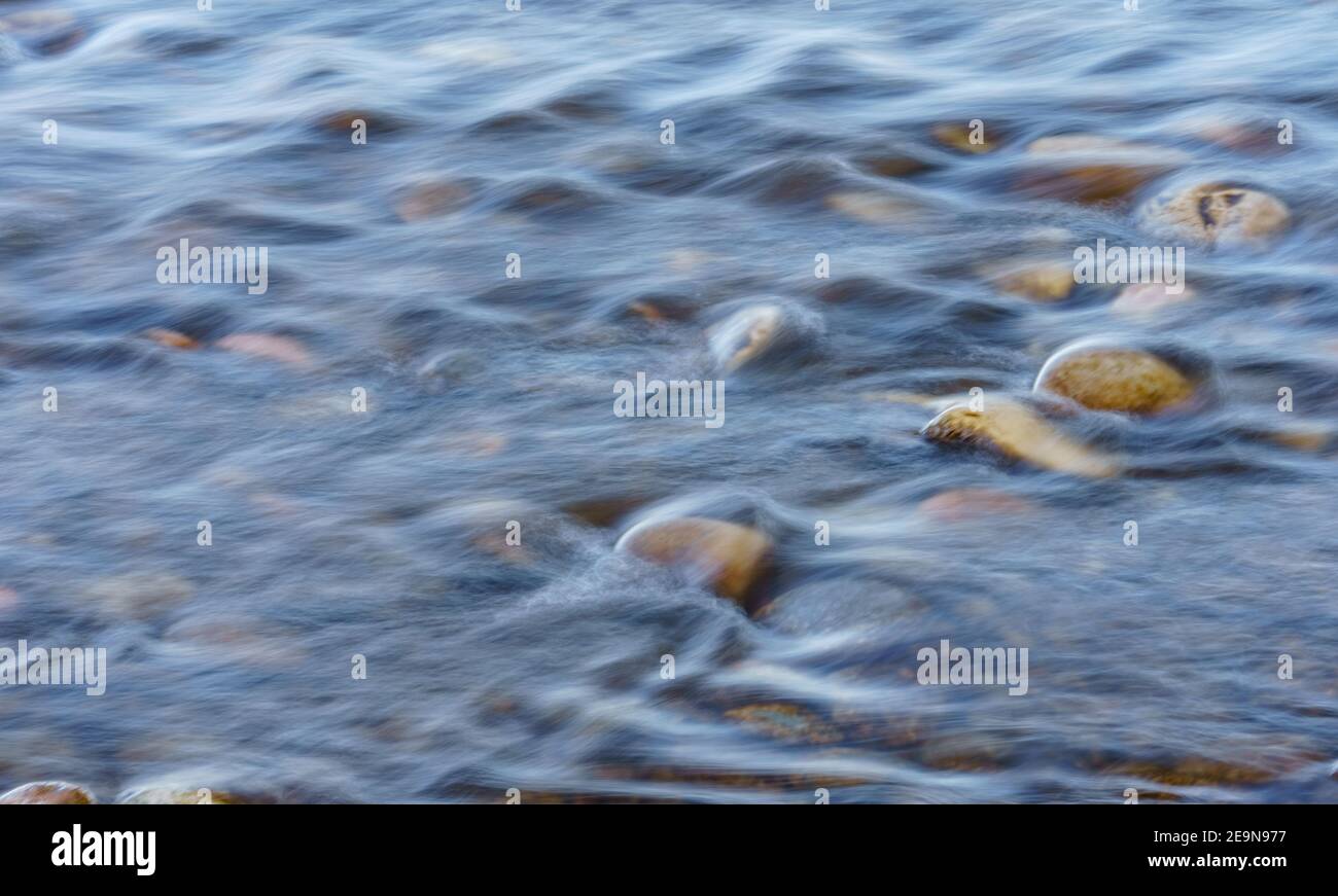 Closeup di riflutti d'acqua sfocati in movimento che scorrono su una pietra di Cobble Letto sul fiume Foto Stock