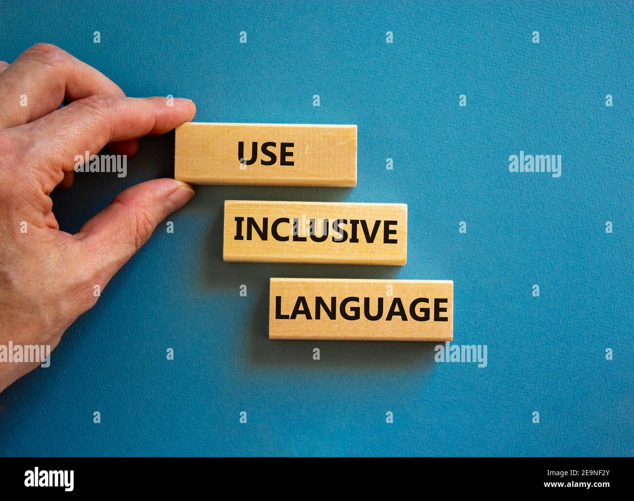 Utilizzare il simbolo della lingua inclusiva. Blocchi di legno con parole 'Use inclusive language'. Bello sfondo blu, mano uomo d'affari. Business e uso inclusi Foto Stock