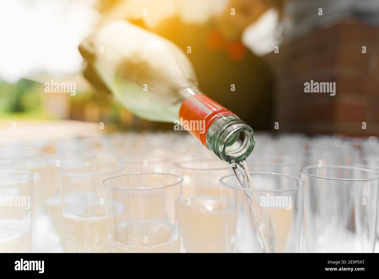 Versare il vino frizzante in un bicchiere da vicino con la luce del sole.  Il cameriere versa le "hamagne" in un bicchiere di vino. Area drink di  benvenuto. Il cameriere in guanti