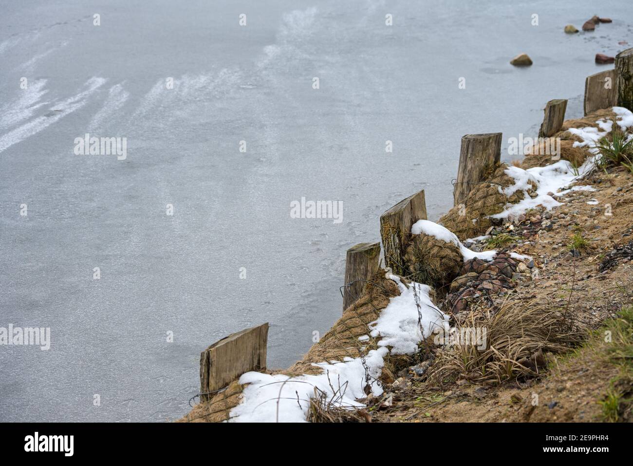 Rinforzo di banca con colonne di legno e balle di paglia in reti su un lago congelato in inverno, spazio di copia, fuoco selezionato, profondità di campo stretta Foto Stock