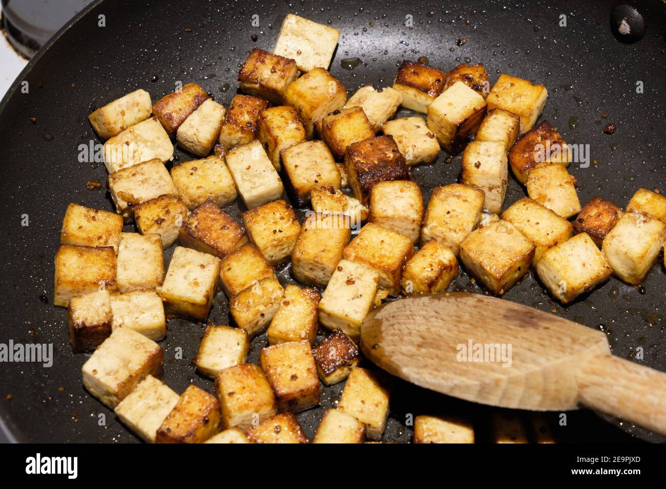 Cubetti marinati di tofu saltati a colori dorati una padella senza bastone Foto Stock