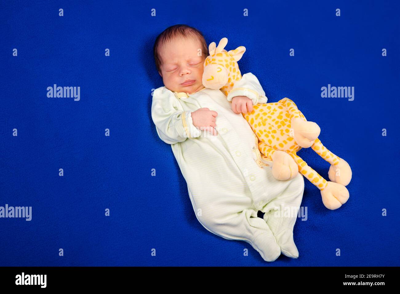 Affascinante neonato sdraiato su una coperta blu con giraffa giocattolo. Ragazzo o ragazza Foto Stock