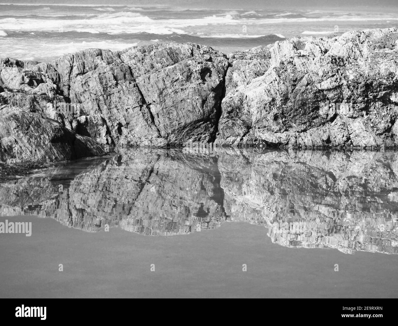 Bei riflessi. Le rocce che confinano con la piscina rocciosa si riflettono e si specchiano nell'acqua salata, guardando oltre l'Oceano Pacifico. Monocromatico Foto Stock