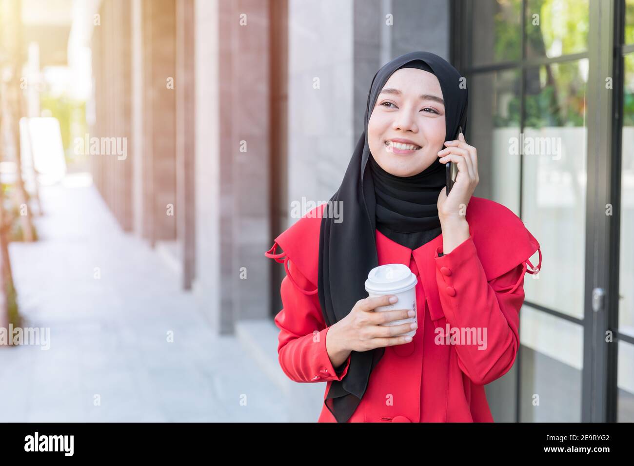 Asian Muslim uomo d'affari felice utilizzando smartphone telefono contatto di chiamata cliente mentre si cammina in strada con una tazza di caffè Foto Stock