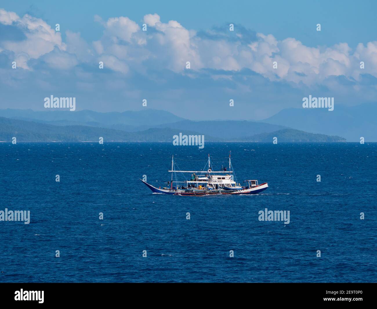 Tradizionale tonniera in legno con gli Outrigger nella Baia di Sarangani sulla strada per il porto di pescatori di General Santos City, con le montagne di Foto Stock