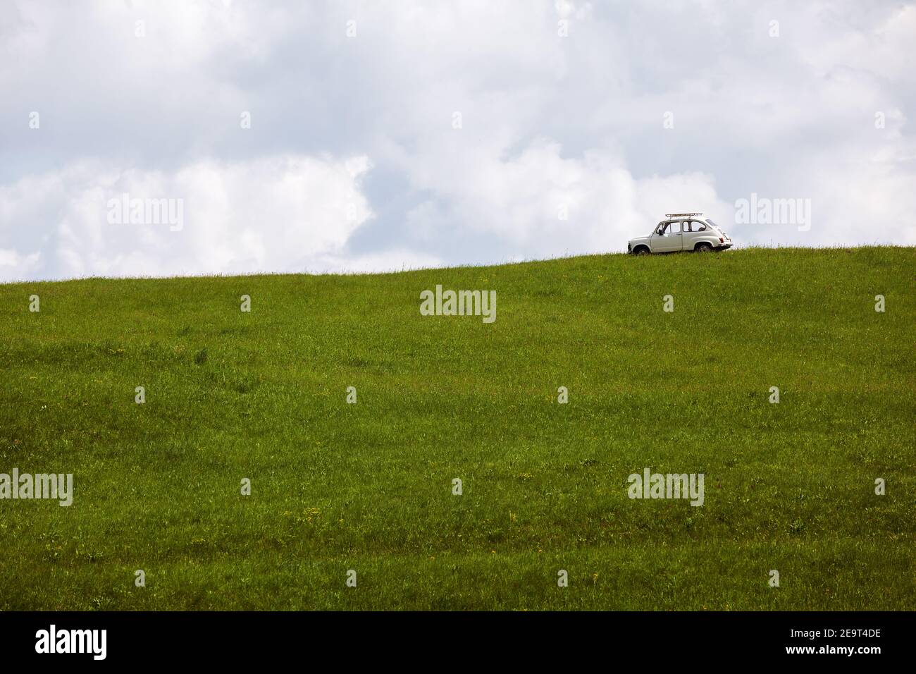 Una vecchia macchina bianca nel mezzo di un prato verde senza erba con un cielo nuvoloso sullo sfondo. Foto Stock