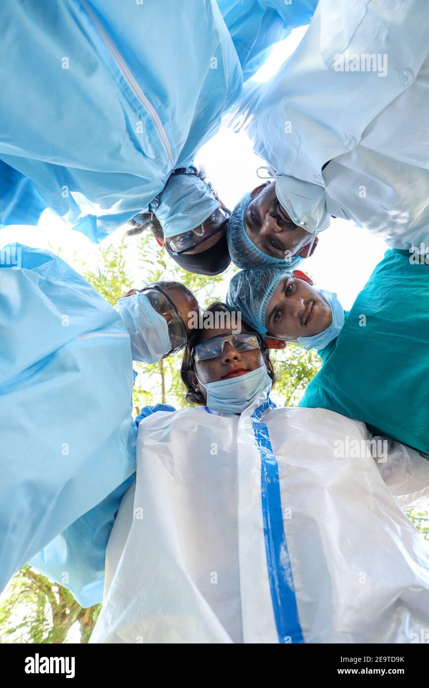 Un colpo basso dell'angolo dei medici indiani che si abbracciano mentre si indossano abiti chirurgici e occhiali di protezione Foto Stock
