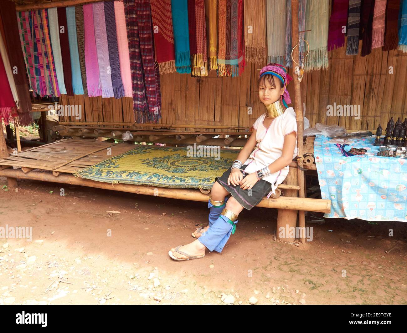 Una bambina della tribù Karen con una collana unica intorno al collo, seduta e appoggiata indietro e in attesa dell'acquirente del suo prodotto tessuto Foto Stock