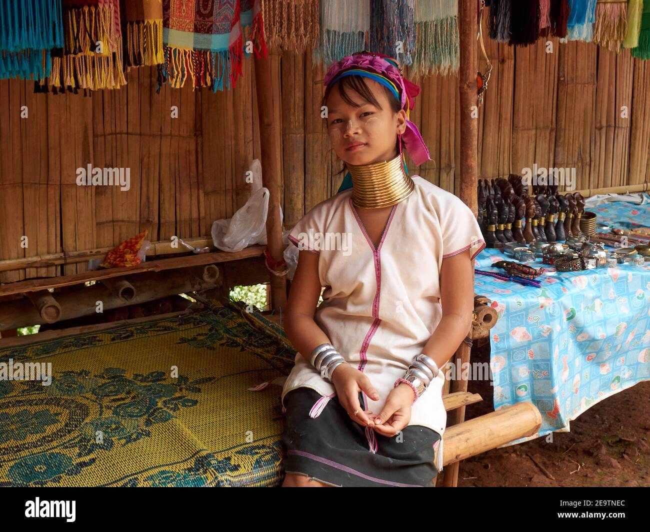 Una bambina della tribù Karen con una collana unica intorno al suo lungo collo, si siede appoggiata indietro e in attesa di acquirenti di prodotti artigianali Foto Stock