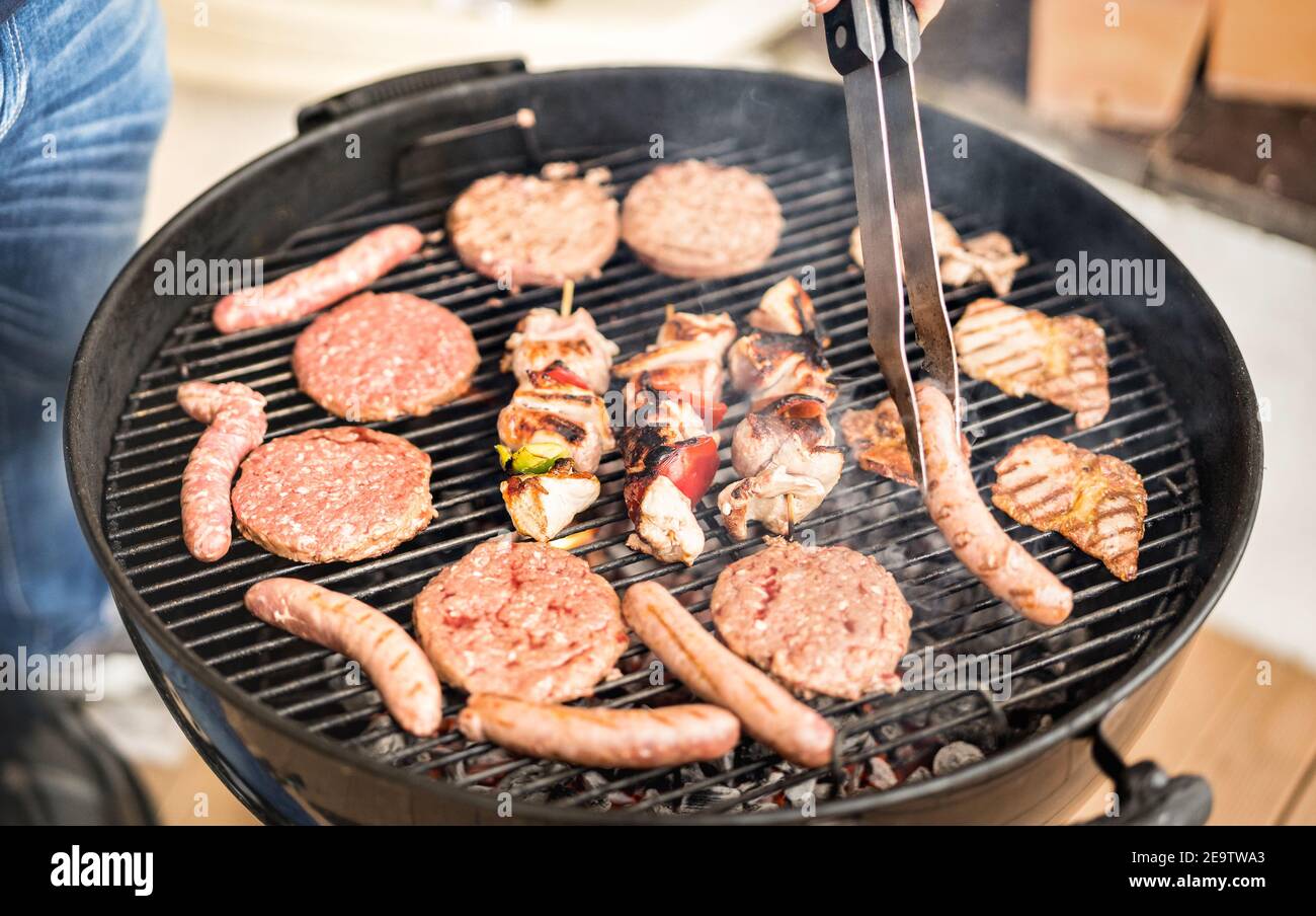 Primo piano di grigliare a mano la carne durante la sessione barbecue - Spiedini e salsicce di hamburger cucinati al barbecue Party - concetto di pic nic Foto Stock