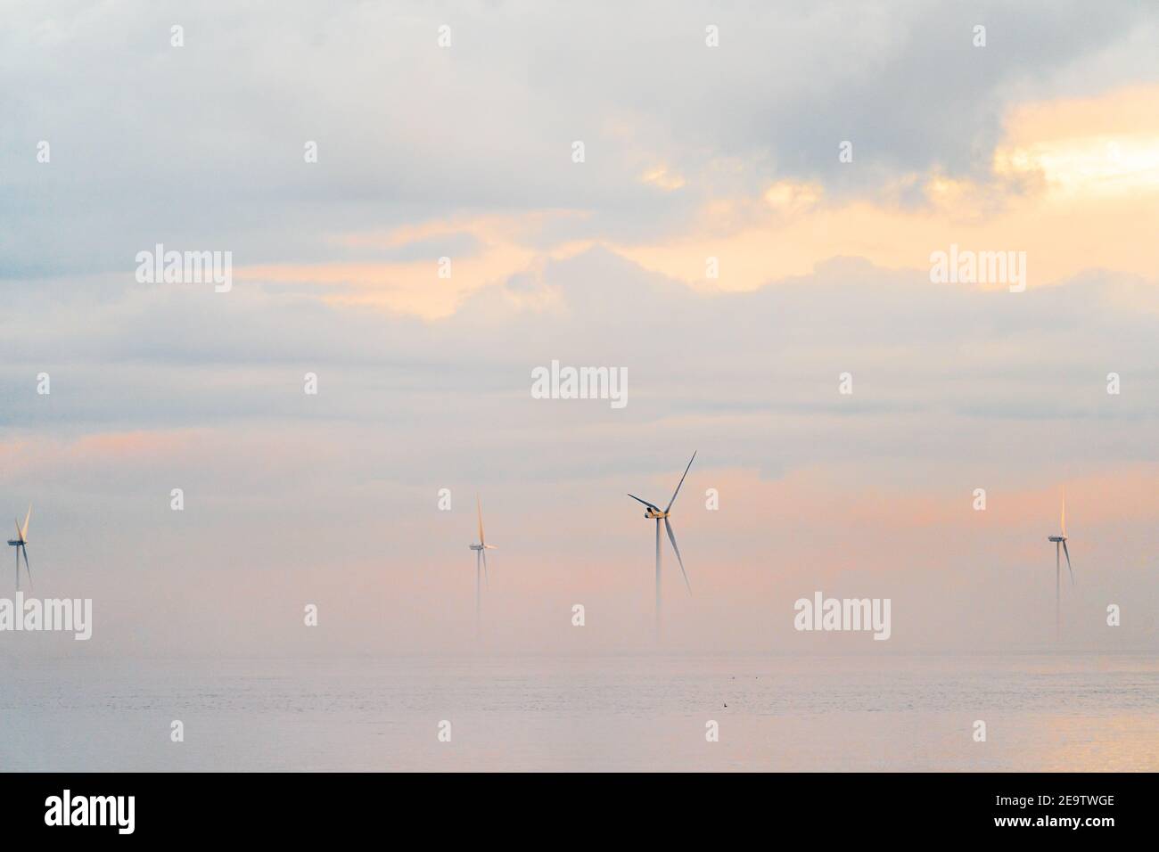 Turbine eoliche del London Array offshore proveniente dall'alba della nebbia mattutina al largo della costa del Kent a Herne Bay. Le cime delle turbine sono visibili con un cielo nuvoloso e grigio con striature arancioni. Il mare è calmo con la nebbia in uno strato sopra di esso. Foto Stock