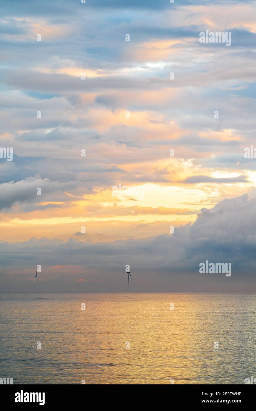 Turbine eoliche del London Array offshore proveniente dall'alba della nebbia mattutina al largo della costa del Kent a Herne Bay. Le cime delle turbine sono visibili con un cielo nuvoloso e grigio con striature arancioni. Il mare è calmo con la nebbia in uno strato sopra di esso. Foto Stock