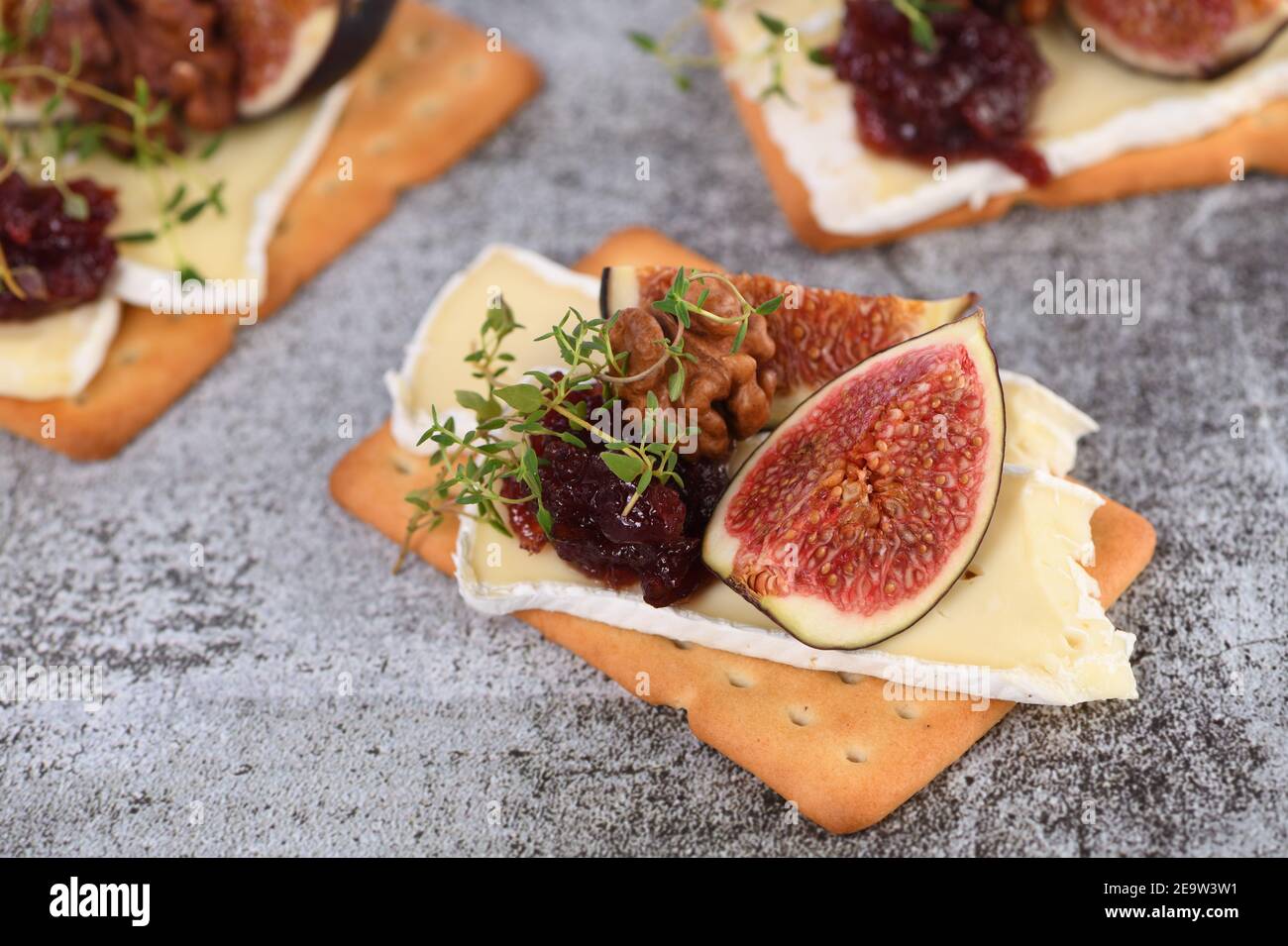 Cracker con una fetta di camembert, marmellata, fichi e noci. Un'ottima idea di spuntino per una vacanza, un picnic o una festa. Foto Stock