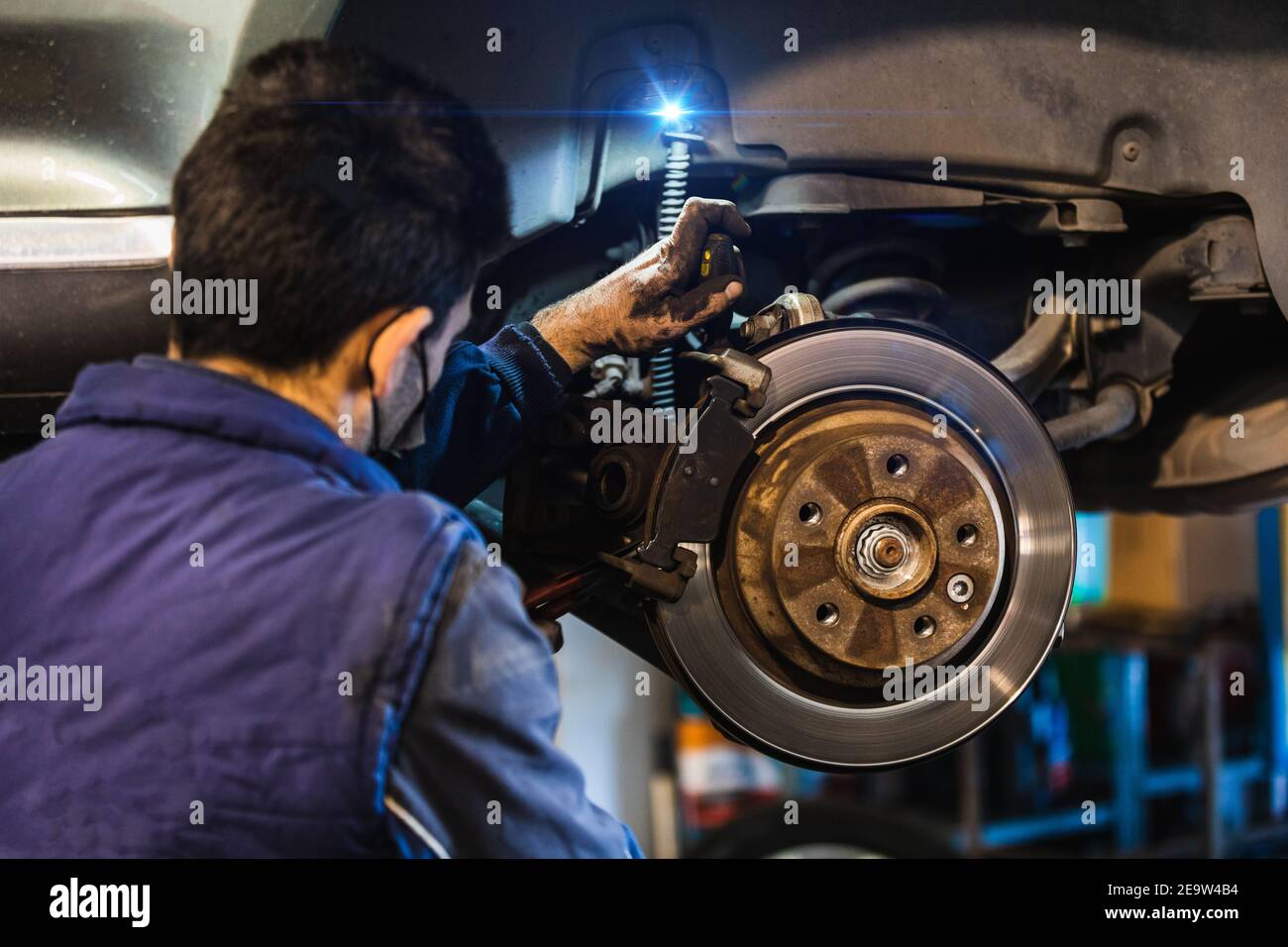 Meccanico che ripara i freni sulla vettura. Maschera. Concetto di riparazione del veicolo con freno a disco di messa a fuoco selettiva Foto Stock