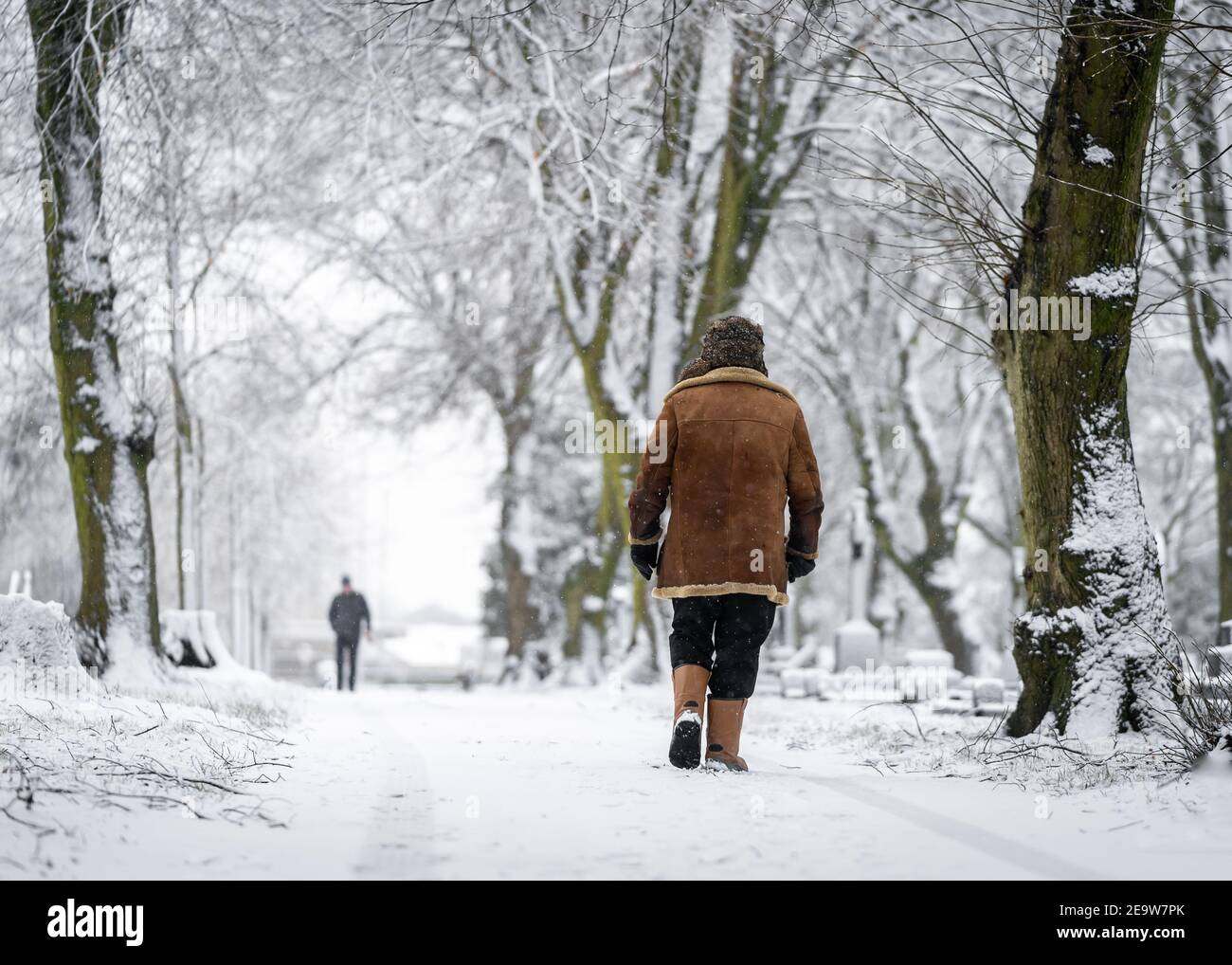 Uomo che cammina lungo il sentiero coperto di neve durante l'inverno avvolto scaldare in cappotto e cappello nella scena locale del villaggio a. Natale condizioni di bizzard con neve fa Foto Stock