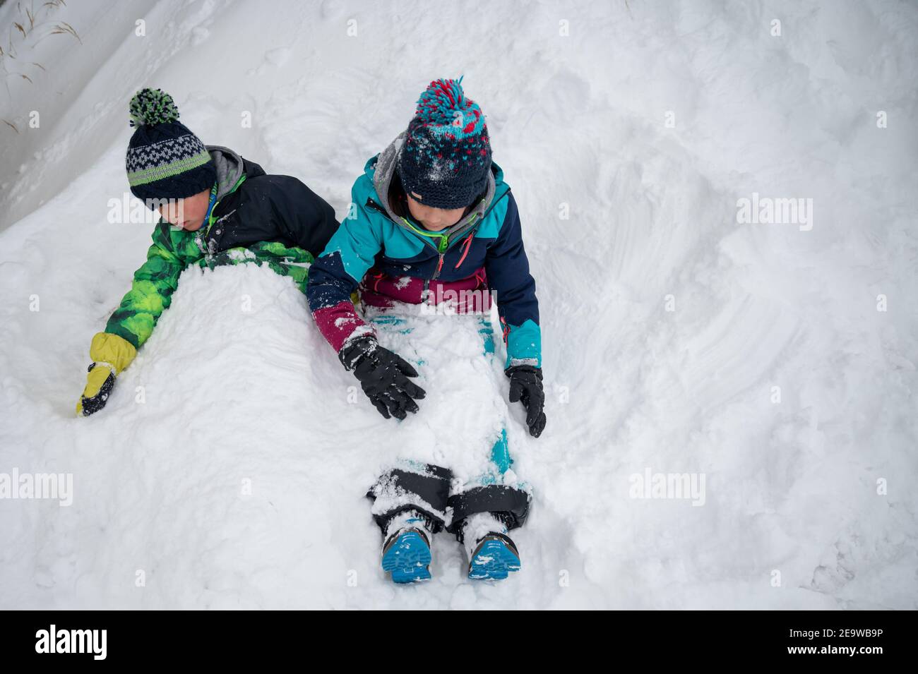 Bambini che giocano nella neve. Due bambini asiatici sepolti nella neve in inverno. Felice infanzia e divertimento. Zermatt, Svizzera. Foto Stock