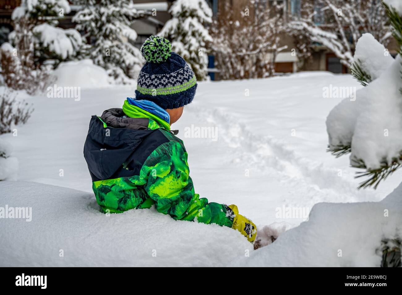 Bambino che gioca nella neve. Un ragazzo asiatico in abbigliamento da sci seduto in inverno. Felice infanzia e divertente. Zermatt, Svizzera. Foto Stock